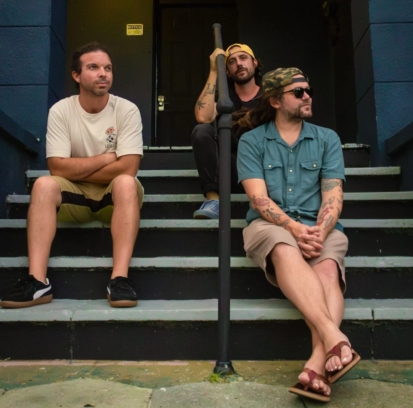 The three members of Algorhythm sitting on the front steps of a blue painted house